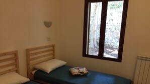 A room with two single beds, a window with a view of a stone wall and trees, and a radiator.