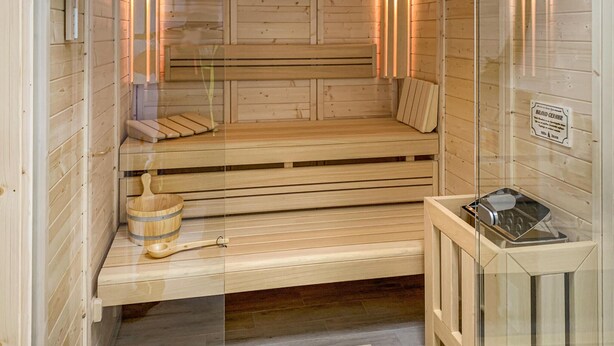 A sauna with wooden benches, a wooden bucket, and a glass-enclosed heater.