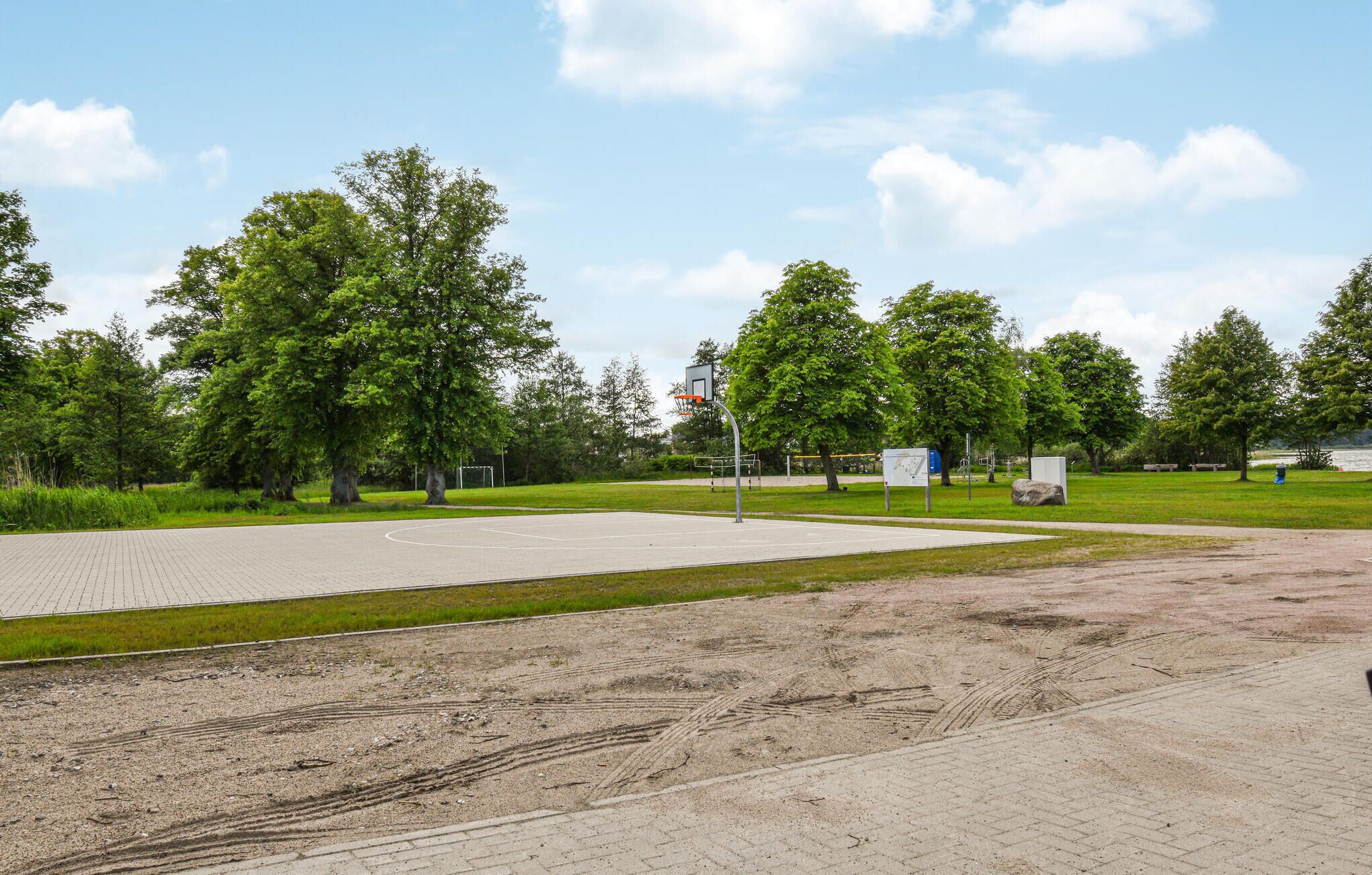 An outdoor basketball court with a hoop, surrounded by trees and a grassy area.