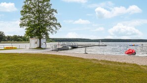 A lakeside dock with a small boat, a lifebuoy, and a lifeboat.
