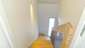 A narrow staircase with wooden steps and a metal railing, leading to a door with a window.