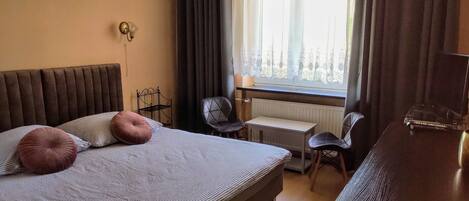 Ein Schlafzimmer mit Bett, zwei Stühlen, einem Schreibtisch, einem Heizkörper und einem Fenster mit Vorhängen.