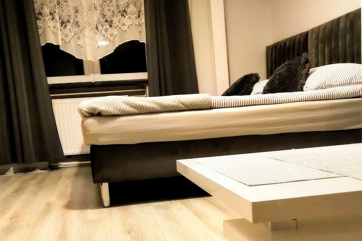 A modern bedroom with a bed, a bedside table, and a window with curtains.