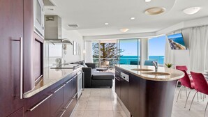 A modern kitchen with a central island, a dining area with red chairs, and a large window overlooking the sea. - Superb location for this level 4  two bedroom apartment, swim between the flags just accross the roa (Mooloolaba)
