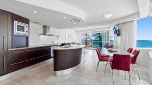 A modern kitchen with a central island, a dining area with red chairs, and a view of the sea. - Superb location for this level 4  two bedroom apartment, swim between the flags just accross the roa (Mooloolaba)
