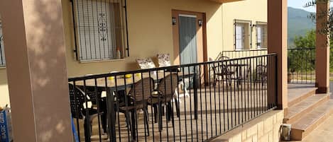 A covered outdoor seating area with a table and chairs, a railing, and a view of the landscape.