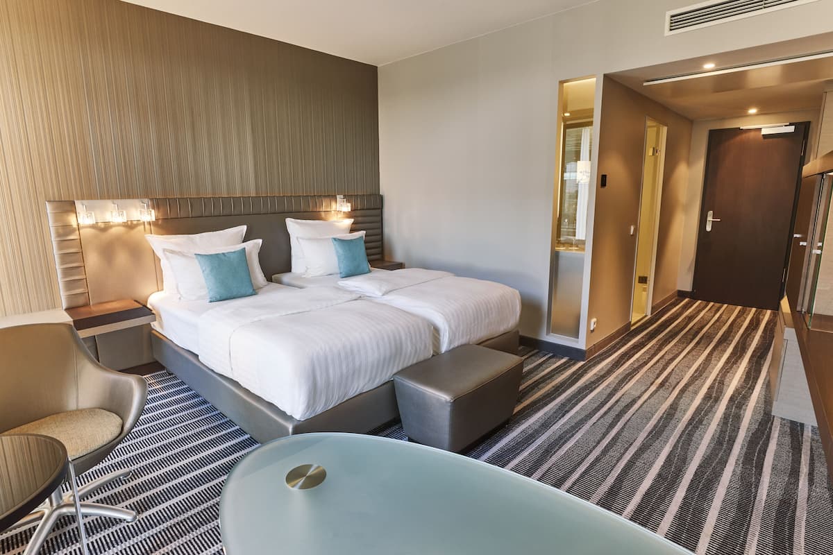 A modern hotel room with a large bed, a sitting area with a chair, a small table, and a bathtub.