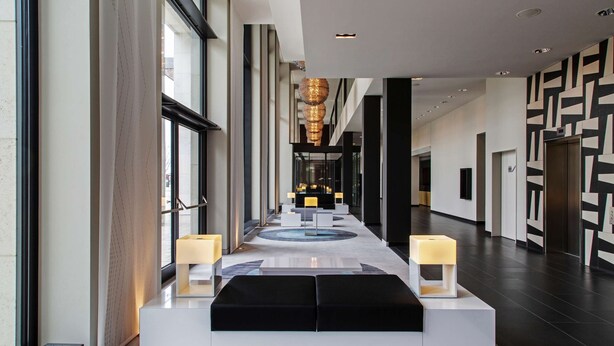A modern hotel lobby with a central seating area, large windows, and a patterned wall design. - Steigenberger Airport Hotel Berlin (Schoenefeld)