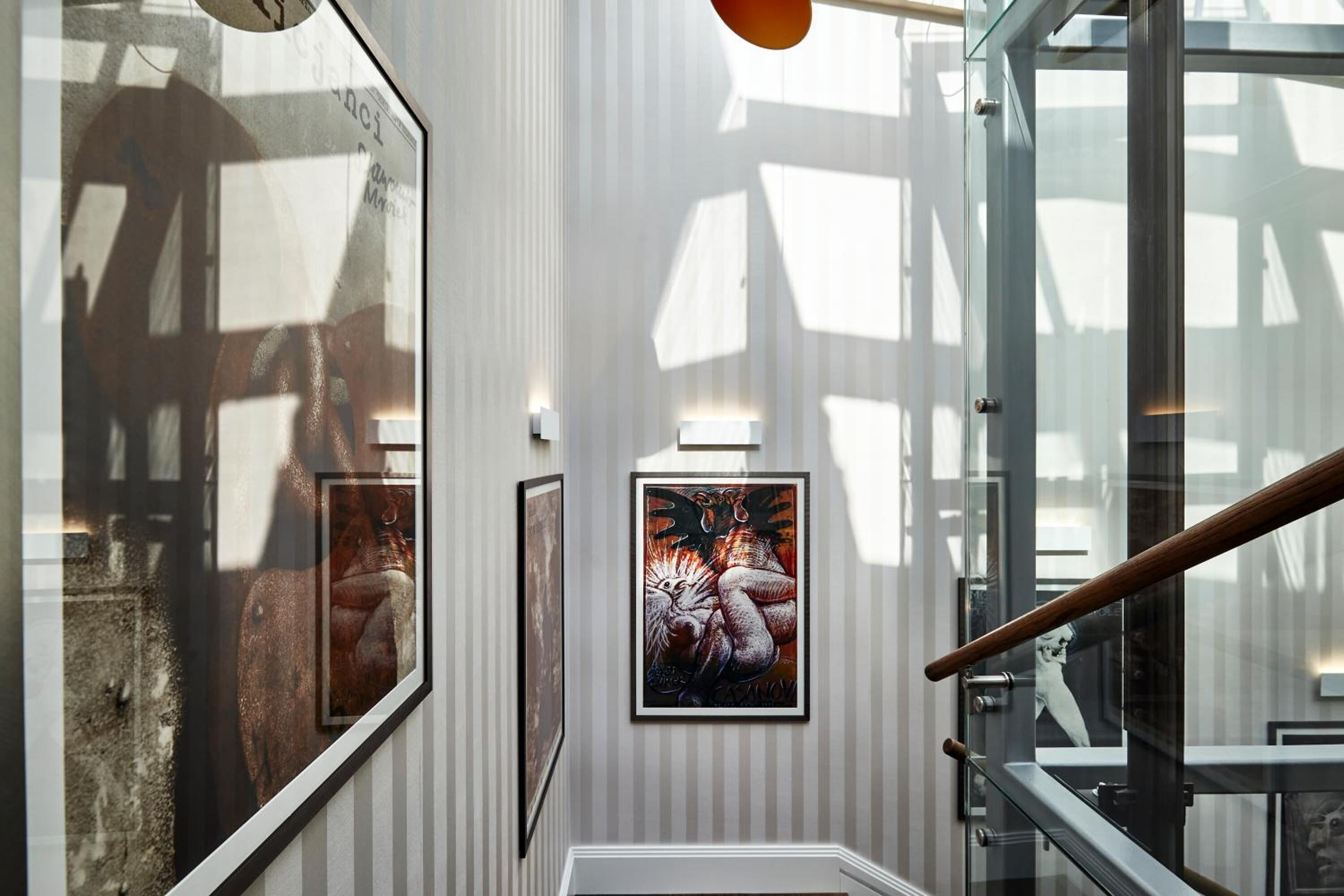 A modern interior with framed artwork on the walls, a glass railing, and a wooden handrail.