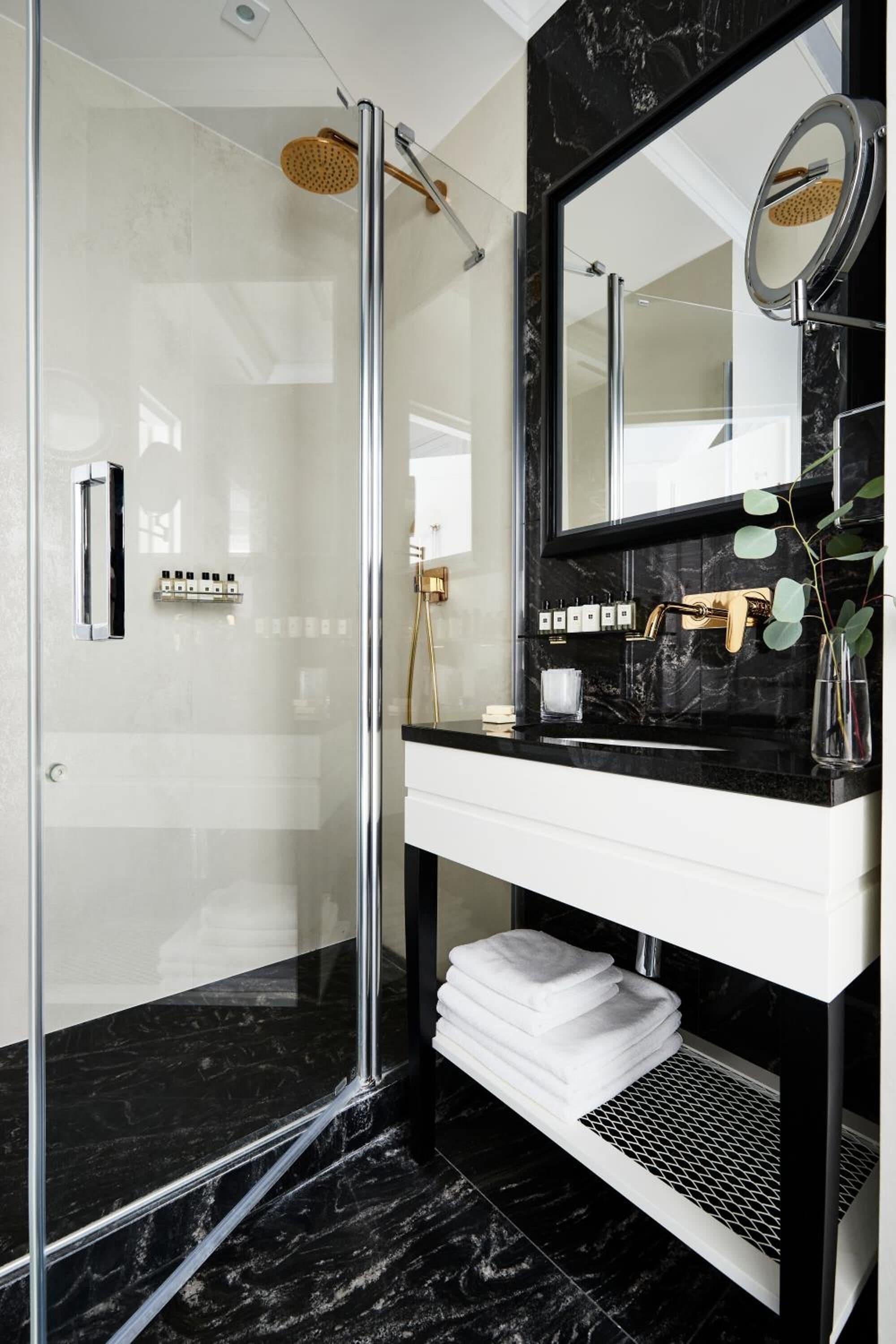 A modern bathroom with a glass-enclosed shower, a black marble countertop, and a white sink.