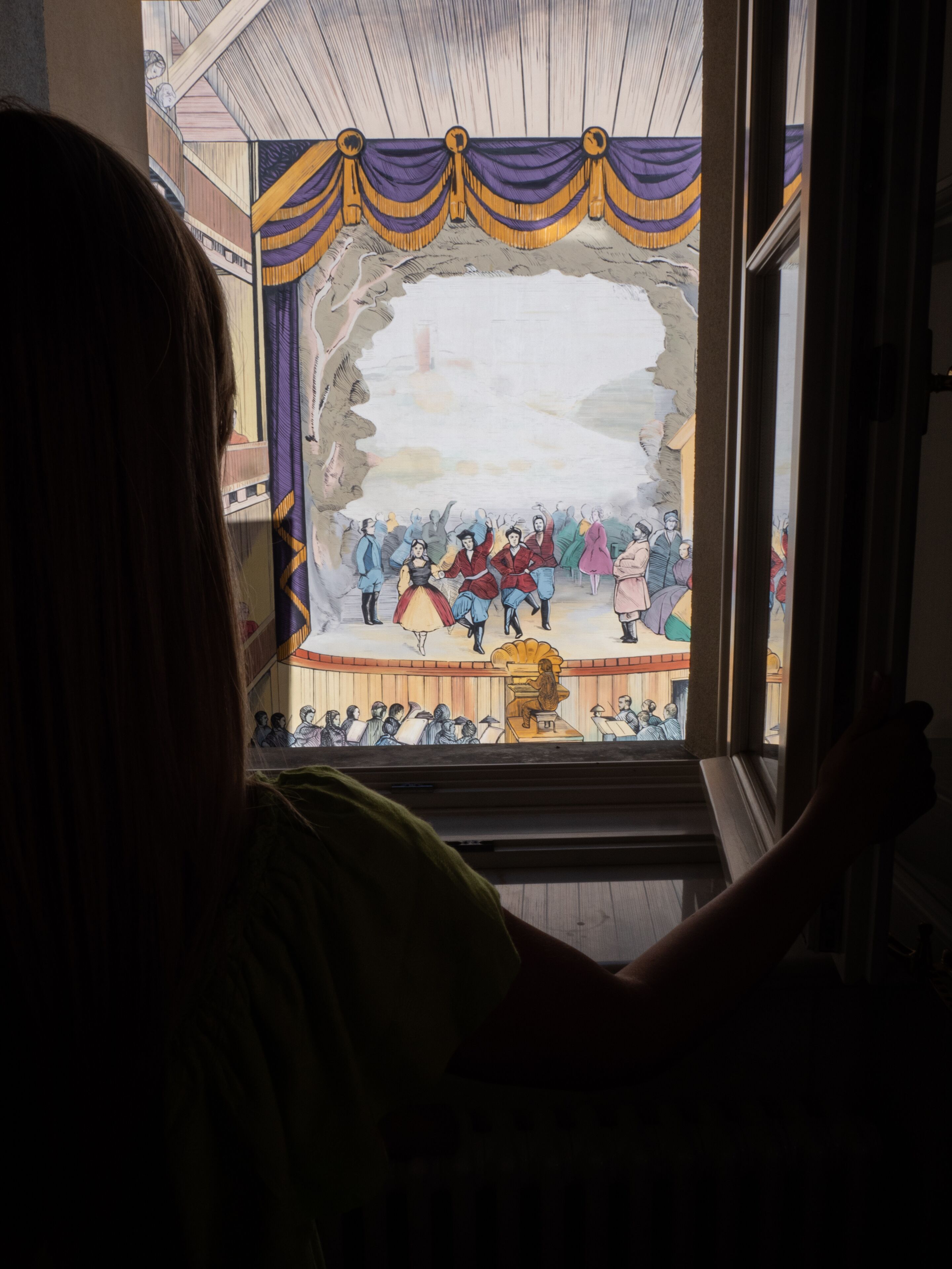 A view through a window of a room with a large stained glass window depicting a historical scene.