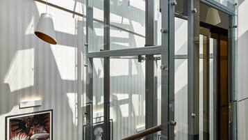 A modern elevator with glass doors and a metal frame, a wooden handrail, and a ceiling light fixture.