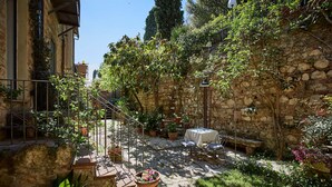 Un patio con muros de piedra, plantas en macetas, una mesa con sillas y un pequeño jardín.