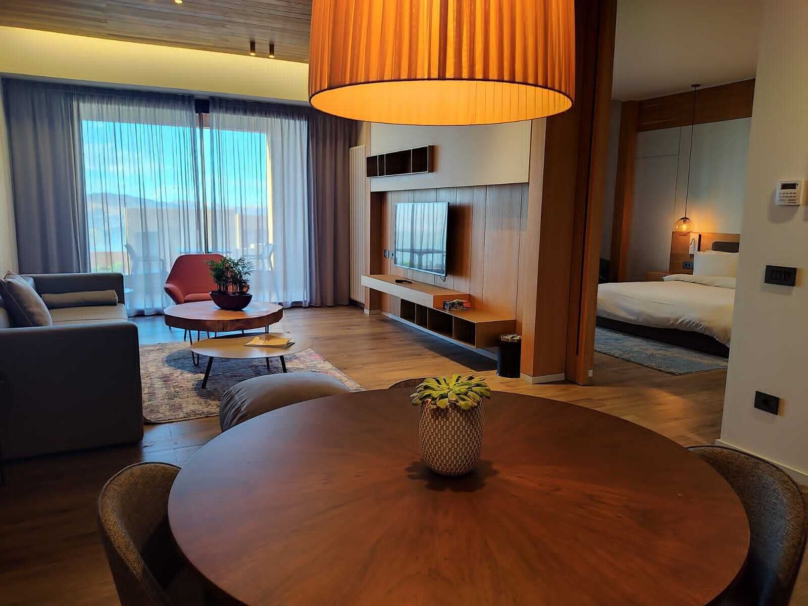 Een moderne woonkamer met een houten eettafel, een bank, een rode fauteuil en een televisie bevestigd aan een houten kast.