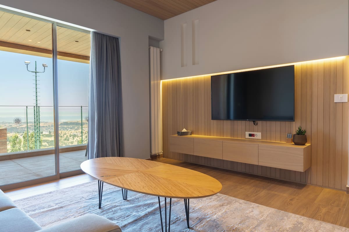 A modern living room with a large TV, wooden paneling, and a view of the outdoors.