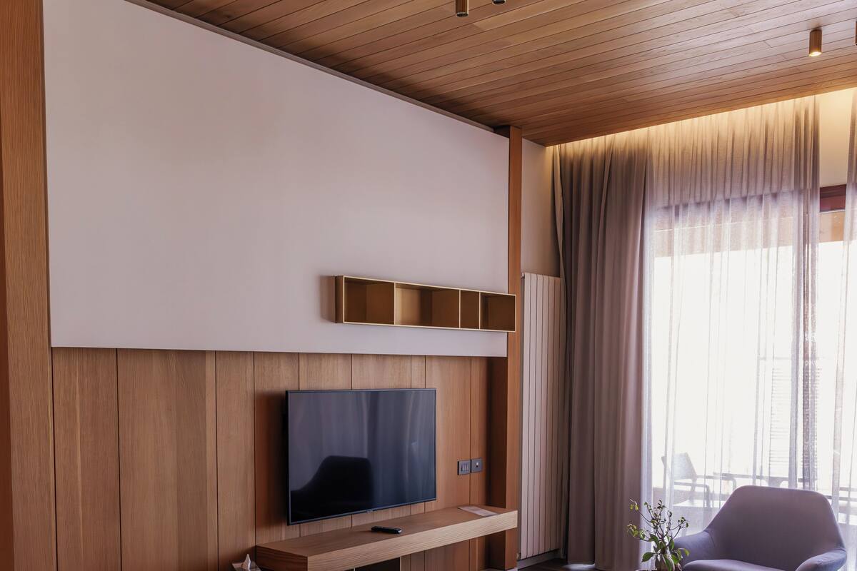 A modern living room with a wooden ceiling, a flat-screen TV, a potted plant, a bean bag, and a grey armchair.