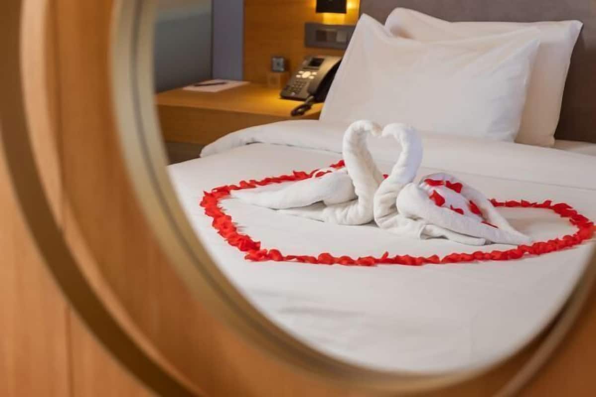 A hotel room with a bed, pillows, a nightstand, a phone, and a wall-mounted lamp.