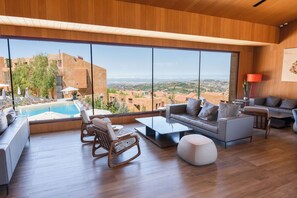 A spacious living area with a large window, a pool, and a view of the surrounding landscape. - Oakridge Hotel & Spa (Mzaar Kfardebian)