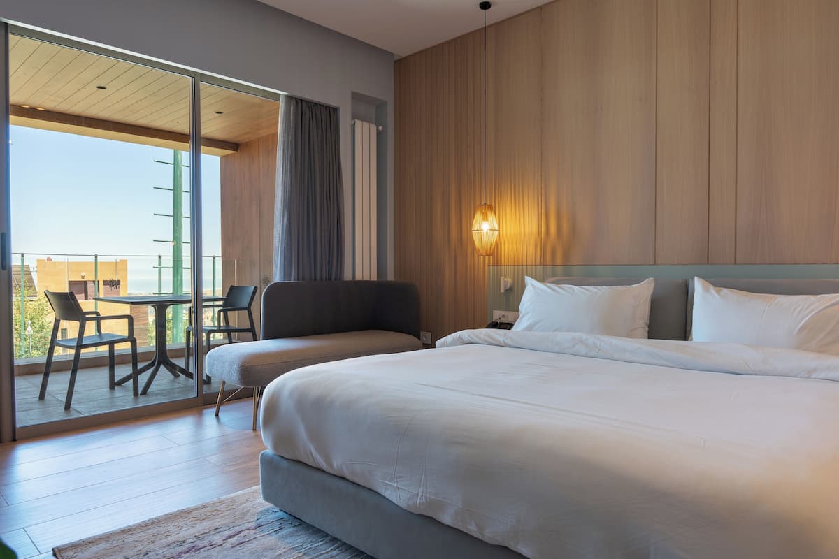 A modern hotel room with a large bed, a seating area with chairs, and a balcony with a view.
