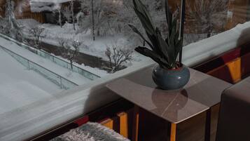 Un interior moderno con vistas a un paisaje nevado, una mesa de madera, un banco y una copa de vino tinto.