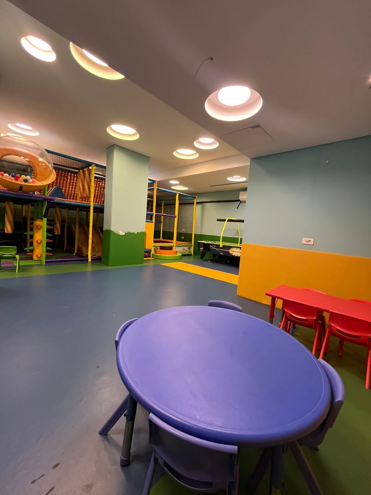 Zona de juegos infantiles con equipo colorido y una mesa con sillas.