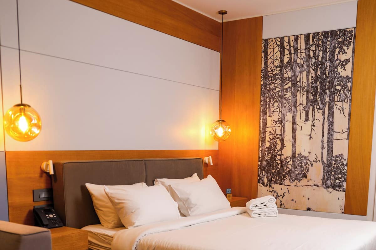 A modern bedroom with a large bed, bedside tables, a desk, and a wall-mounted painting.