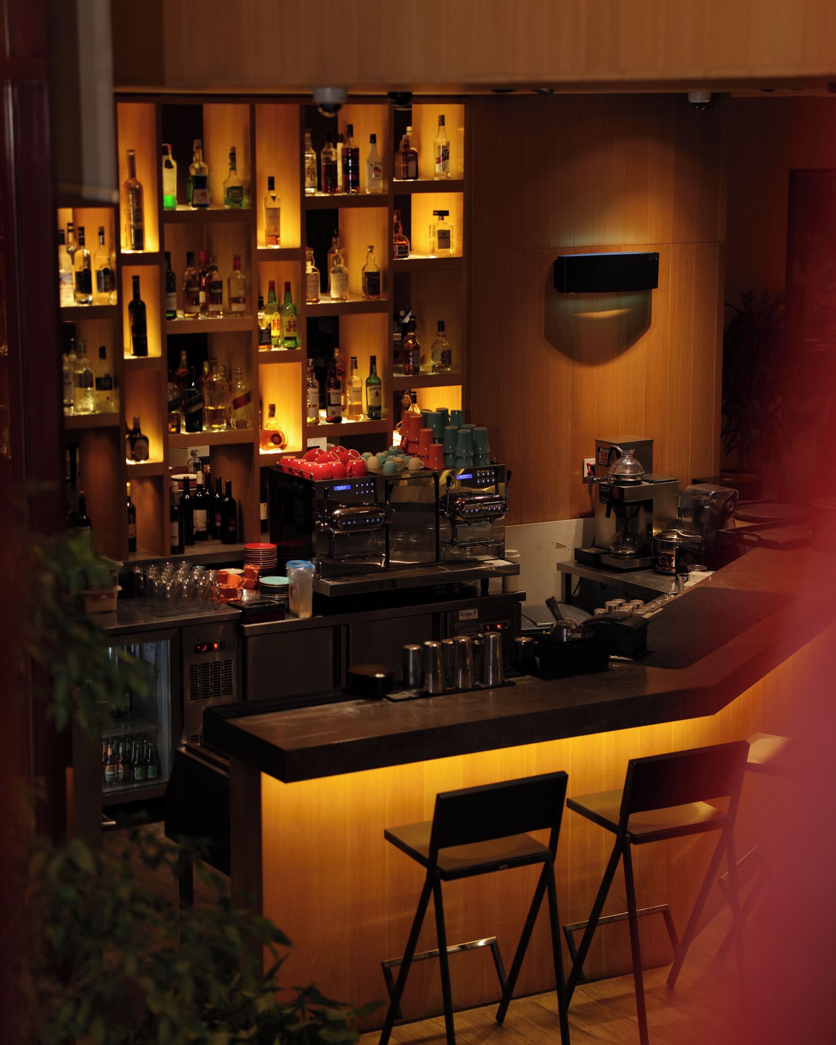 A bar area with shelves of bottles, a coffee machine, and bar stools.