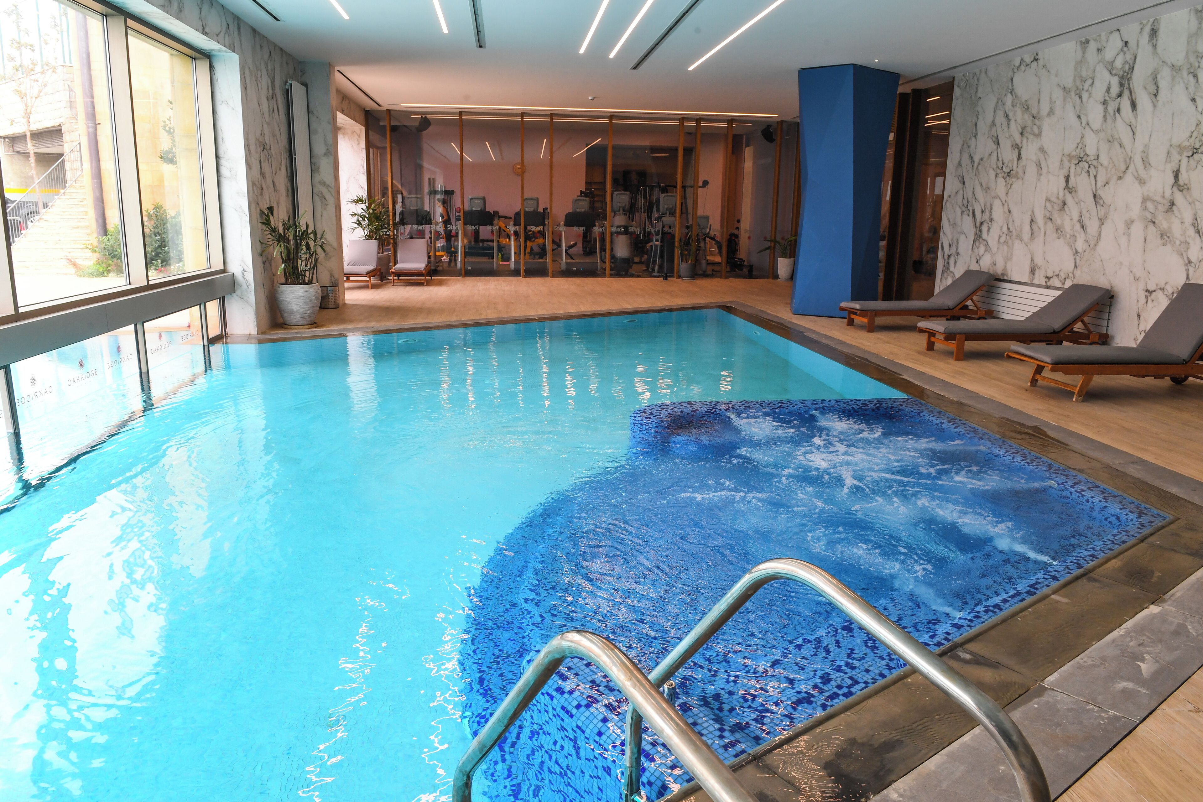 Una piscina interior amb aigua transparent i blava, un solàrium amb rajoles i gandules.