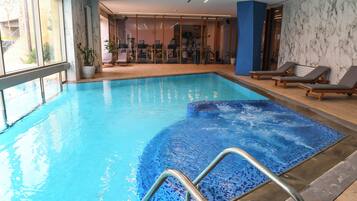 Una piscina interior amb aigua transparent i blava, un solàrium amb rajoles i gandules.