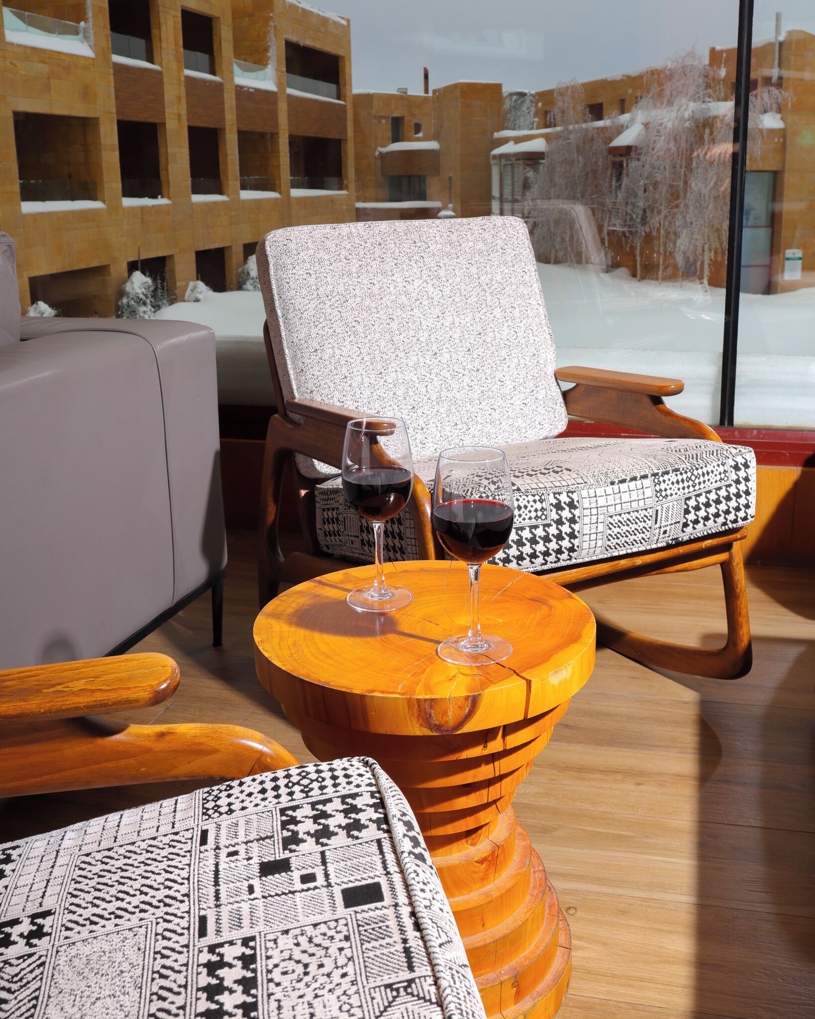 A cozy seating area with a cushioned chair, a wooden side table with two wine glasses, and a patterned rug.