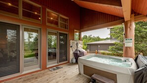 A wooden deck with a hot tub, large sliding glass doors, and a stone fireplace. - Dog Friendly Mountain Retreat w/ Hot Tub & Views (McHenry)