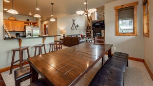 A spacious kitchen with a long wooden table, bar stools, and pendant lighting. - Dog Friendly Mountain Retreat w/ Hot Tub & Views (McHenry)