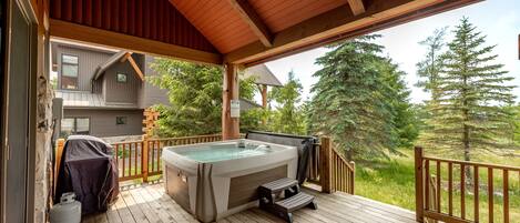 Una terraza de madera con jacuzzi, parrilla cubierta y un escalón que lleva a una casa.