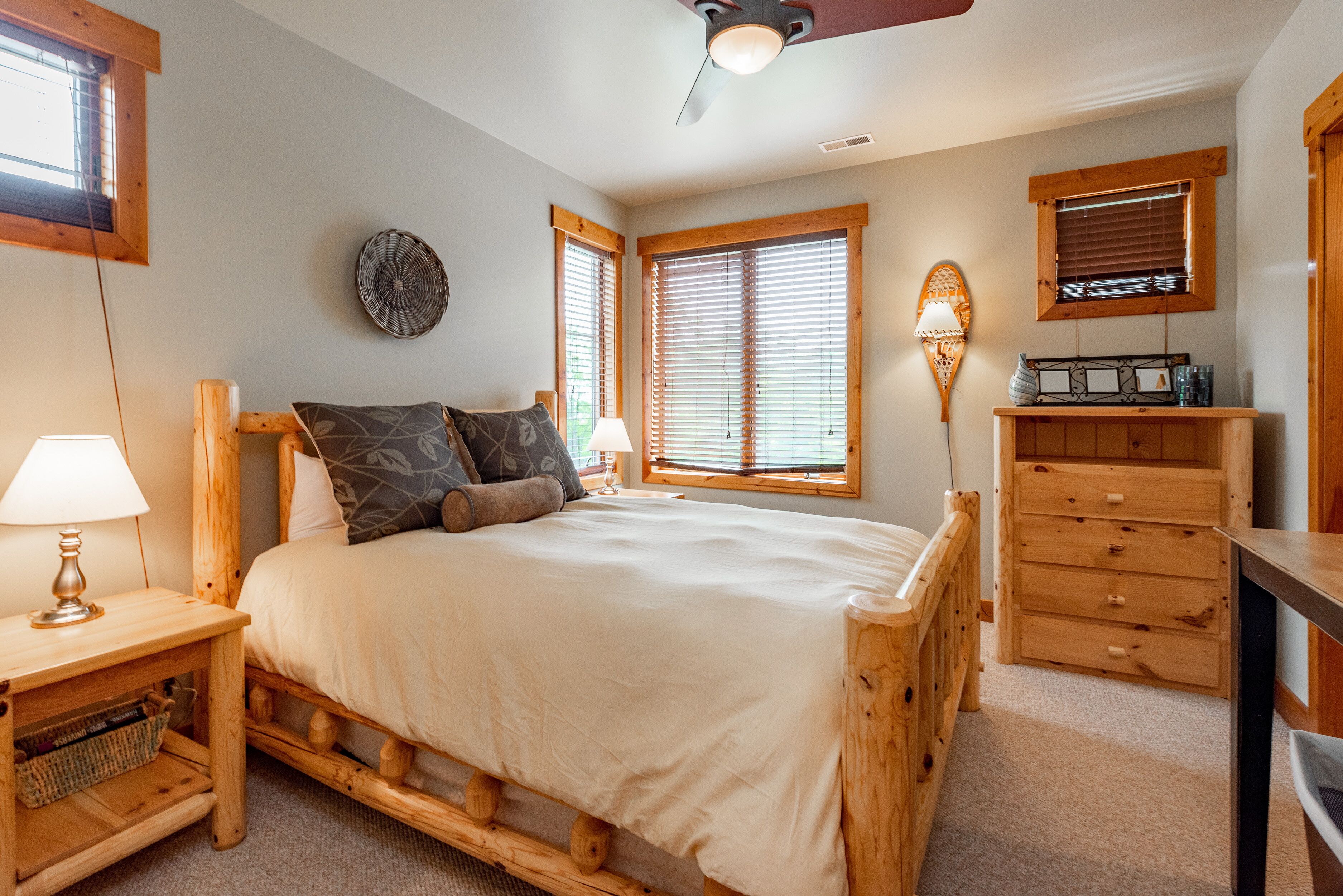 Une chambre à coucher avec un lit en bois, deux tables de chevet avec des lampes, une commode et un ventilateur de plafond.