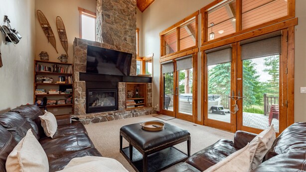 A cozy living room with a stone fireplace, leather sofas, and a large window offering a view of the outdoors. - Dog Friendly Mountain Retreat w/ Hot Tub & Views (McHenry)