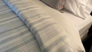 Ein ordentlich bezogenes Bett mit Streifenmuster, eine Lampe und eine Wanduhr.