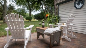 Eine Terrasse mit zwei Adirondack-Stühlen, einem Holztisch und einer Weinflasche.