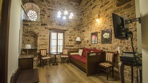 Una habitación con paredes de piedra, suelo de madera, un sofá rojo, sillas a rayas, una mesita y una lámpara en el techo.
