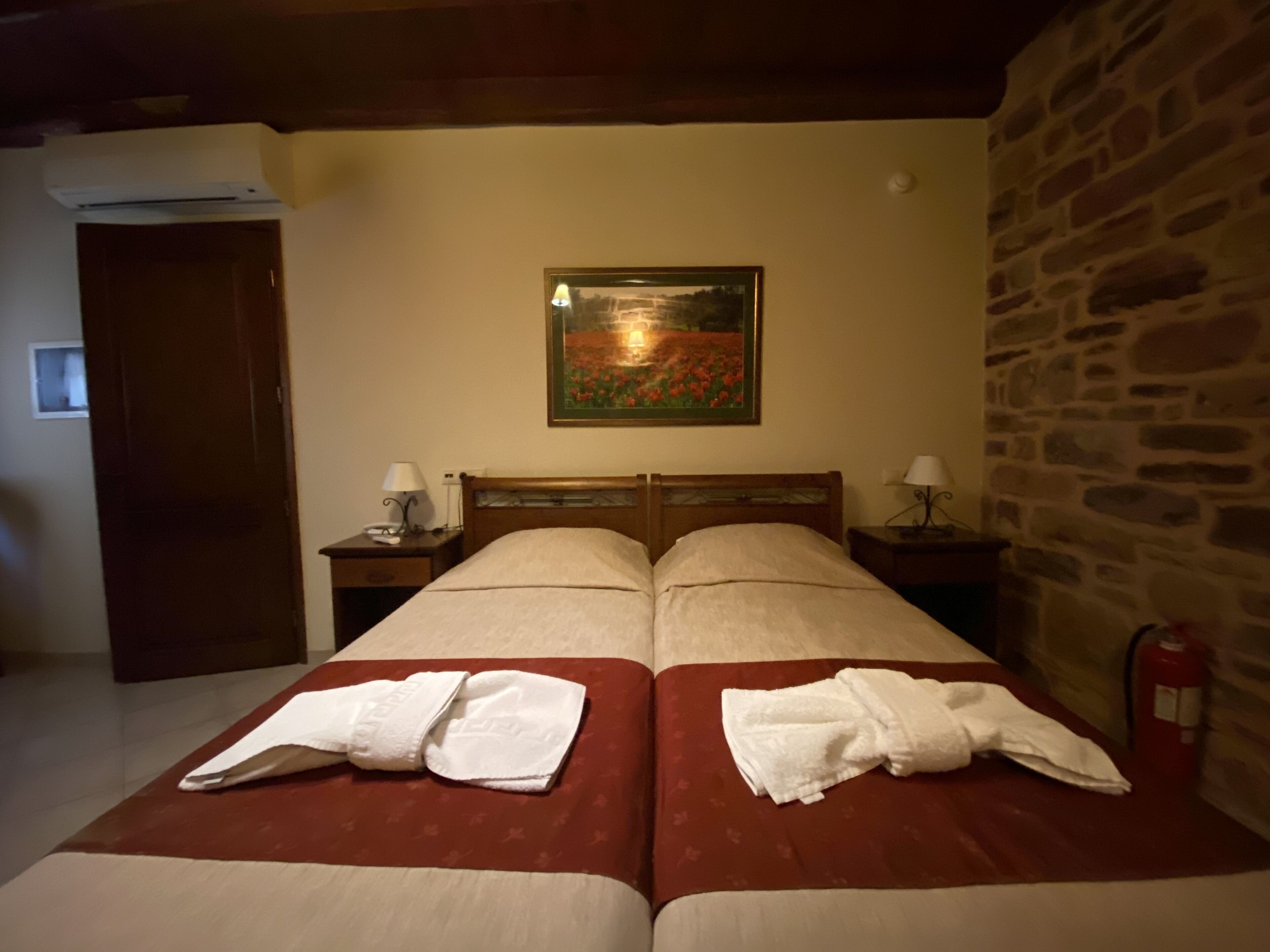 Een hotelkamer met twee bedden, een schilderij aan de muur, een stenen muur en een brandblusser.