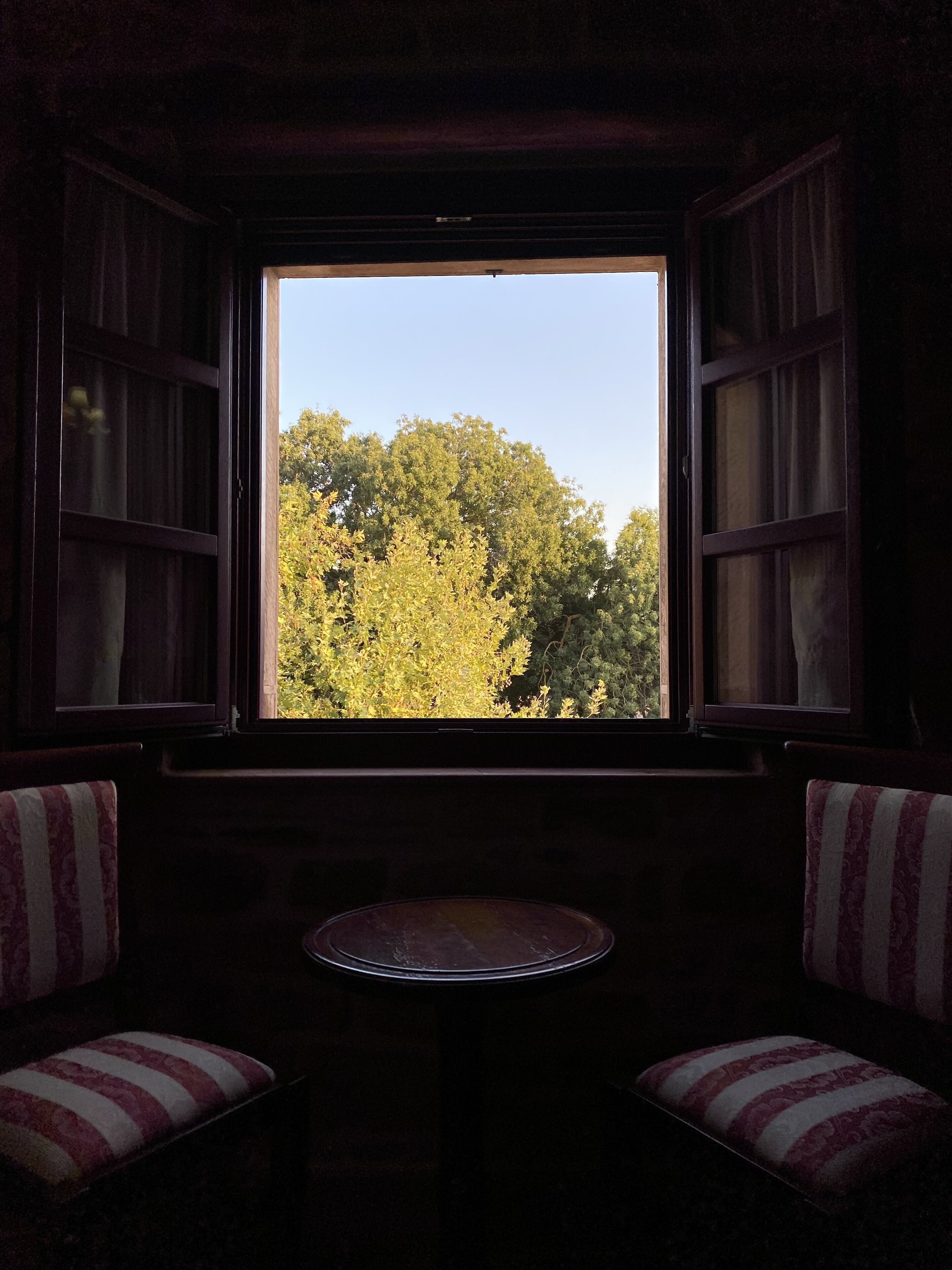 Una habitación con ventana, dos sillas a rayas y una mesita.