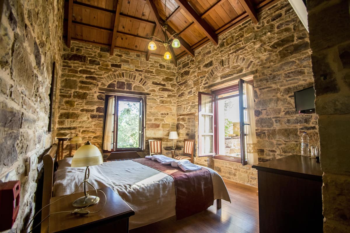 A stone-walled room with a bed, a desk, a lamp, and a television.