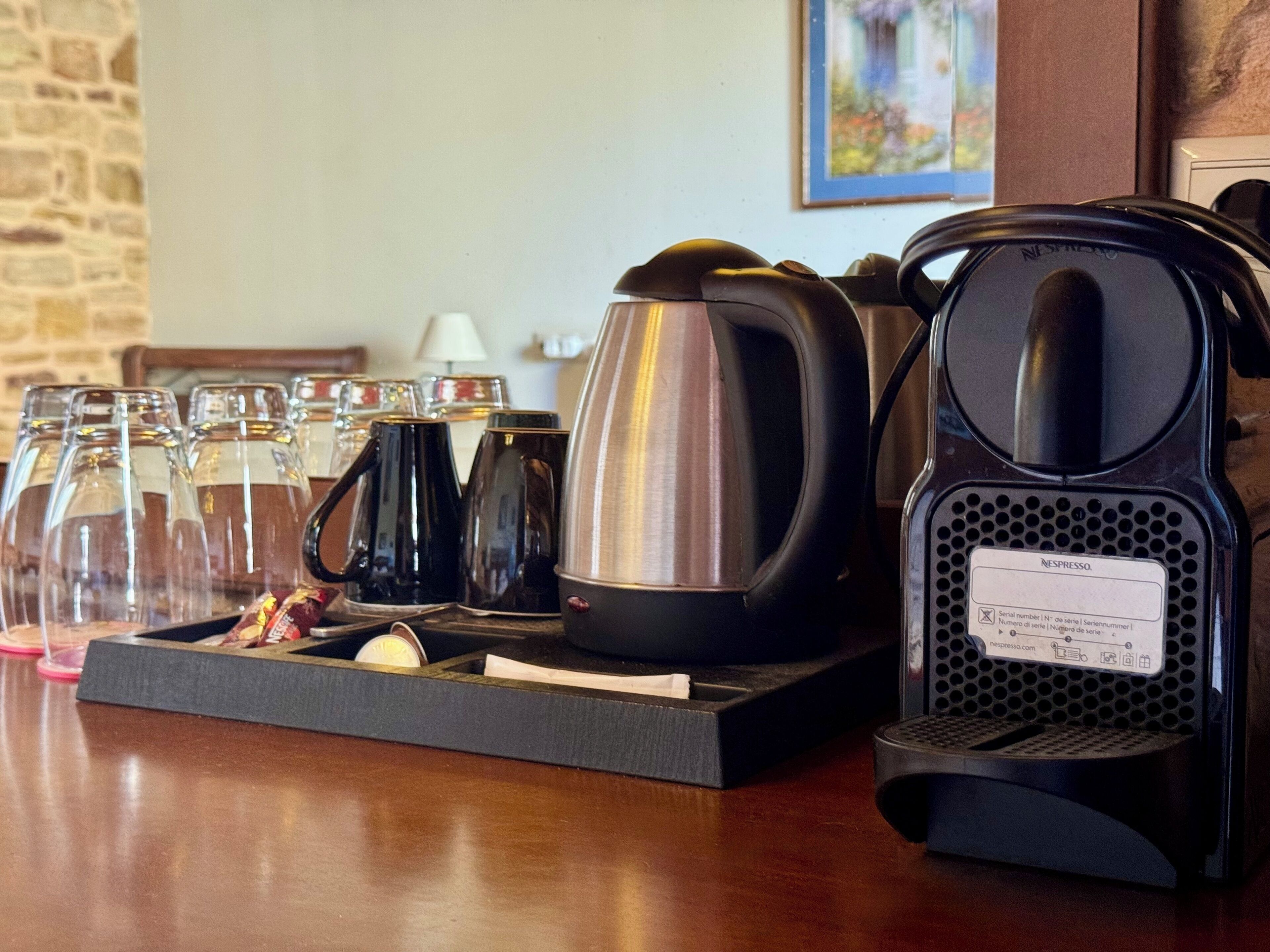 Una estación de café con una cafetera, un hervidor y varias tazas y vasos sobre una bandeja.