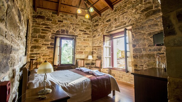 Dormitorio con paredes de piedra, una cama, un escritorio y una ventana con vistas a zonas verdes.
