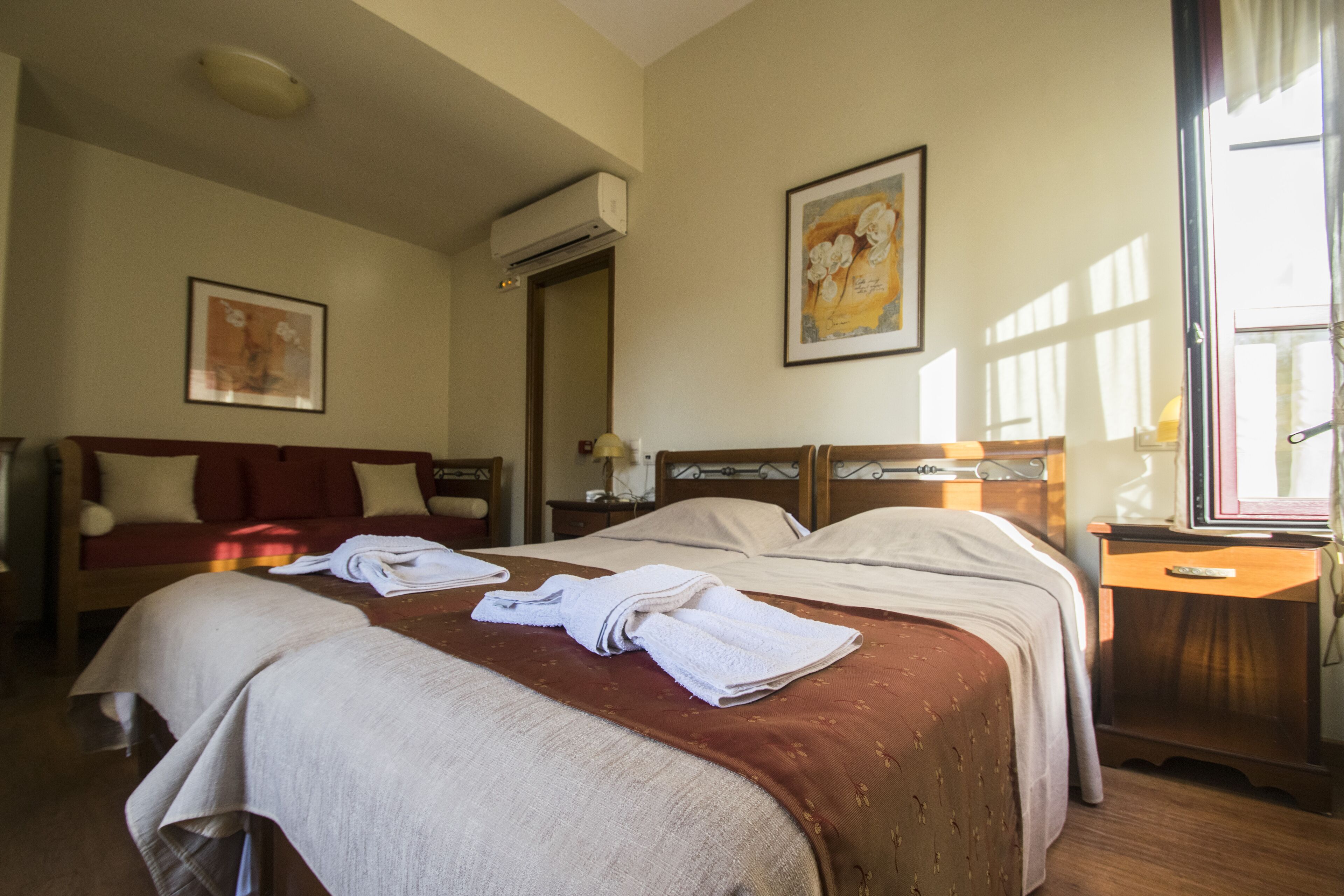 Una camera d'albergo con due letti, un'area salotto, una finestra e un quadro appeso al muro.