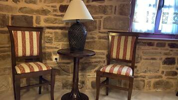 Two wooden chairs with striped upholstery, a table with a lamp, and a stone wall background.
