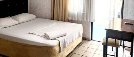 Een hotelkamer met een bed, bureau en raam met gordijnen.