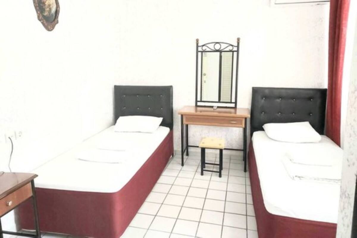 A small, clean room with two single beds, a desk, and a mirror.
