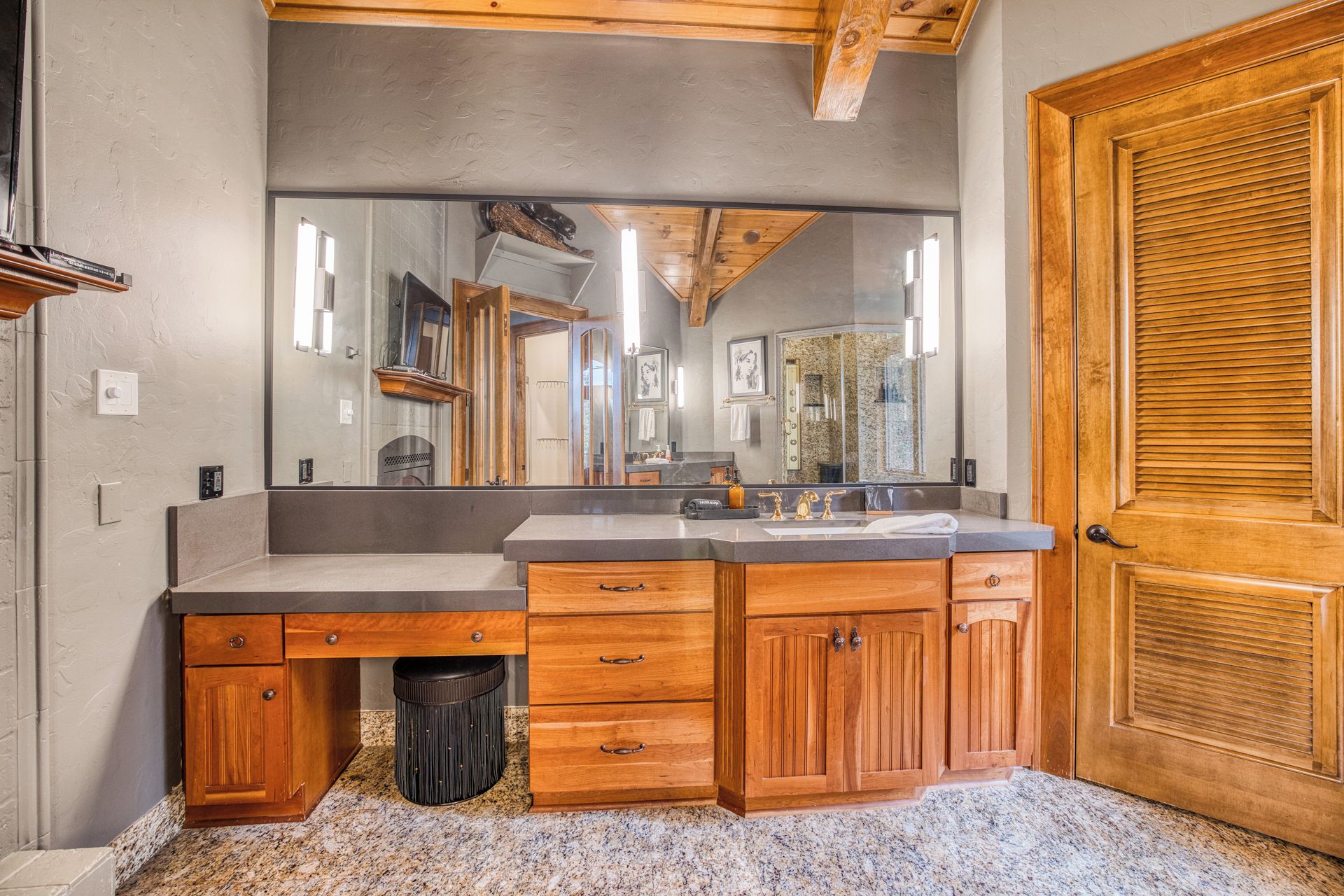 A bathroom with a wooden vanity, a large mirror, and a wooden door.