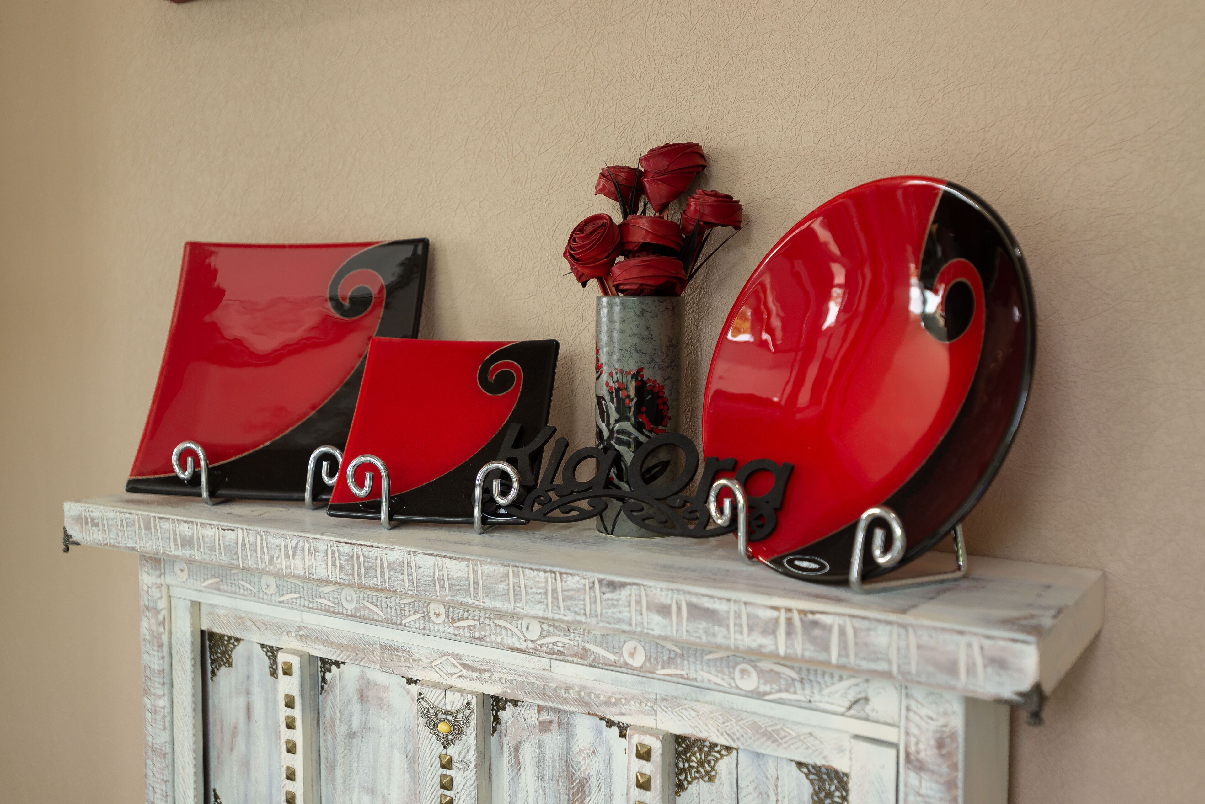 A fireplace mantel with decorative plates and a vase of red roses.