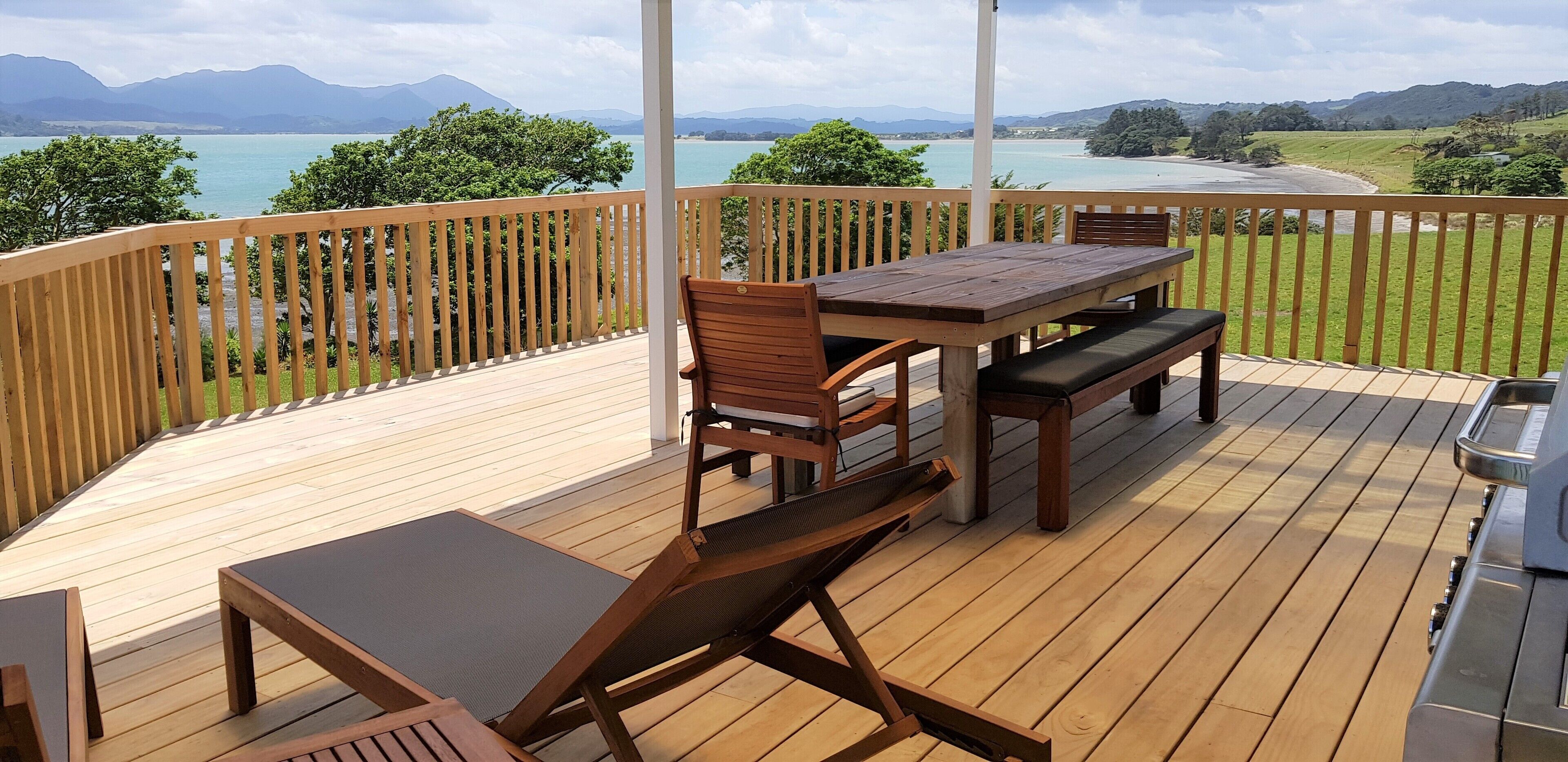 Una terraza de madera con una mesa y sillas, con vistas panorámicas a un lago y montañas.